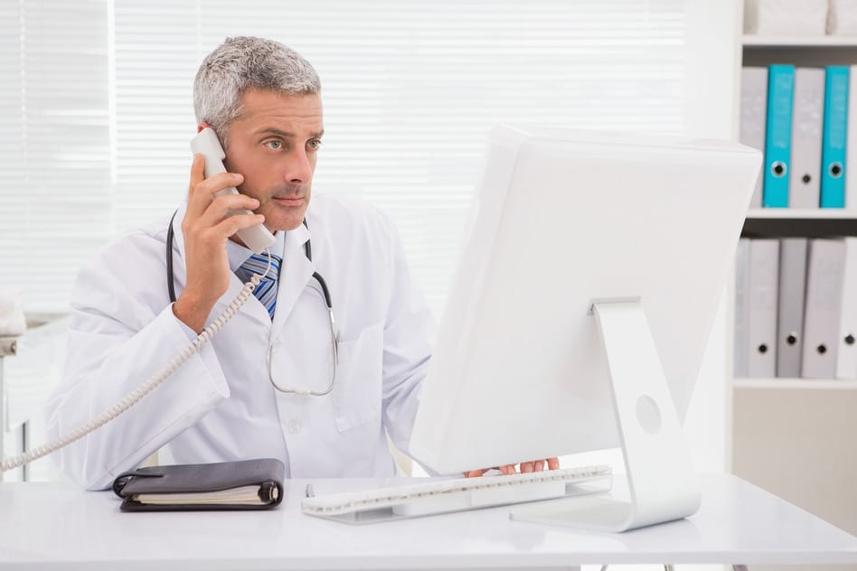 Doctor phoning and using computer in medical office